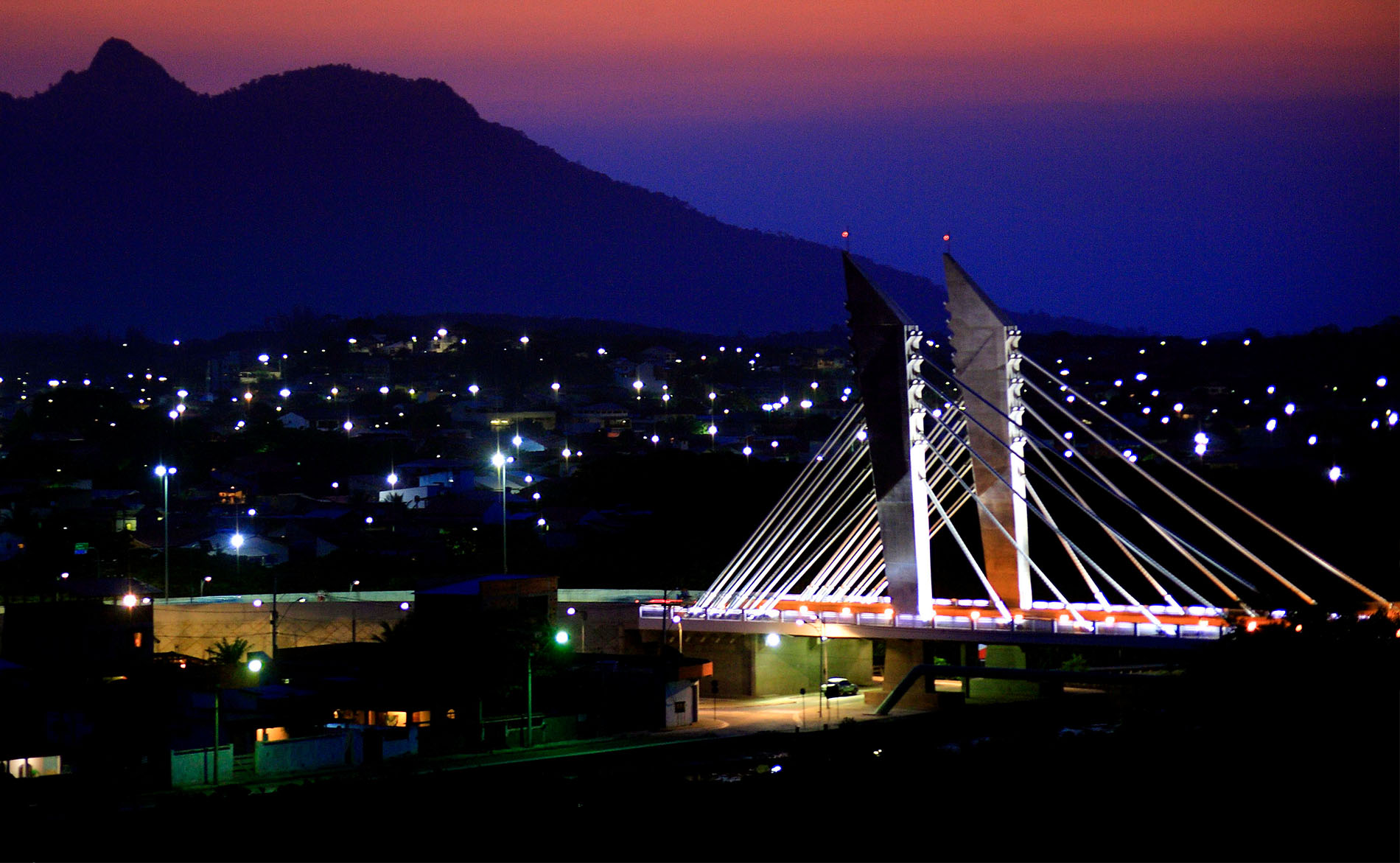 Foto do inicio da noite na cidade, com a ponte ao fundo